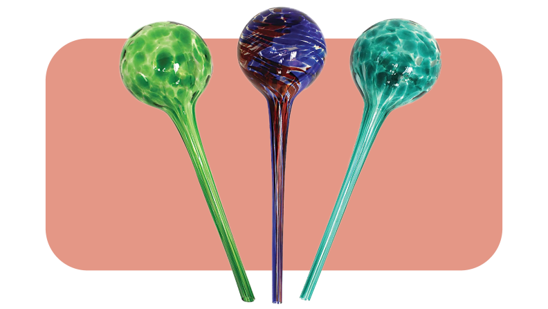 Set of three glass watering globes in green, red and blue and turquoise colors in front of pink background.