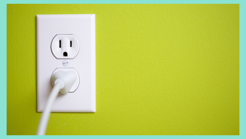 White cord plugged into an outlet on a chartreuse color wall.
