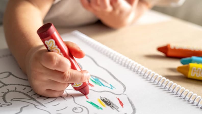 A child colors with a red crayon.