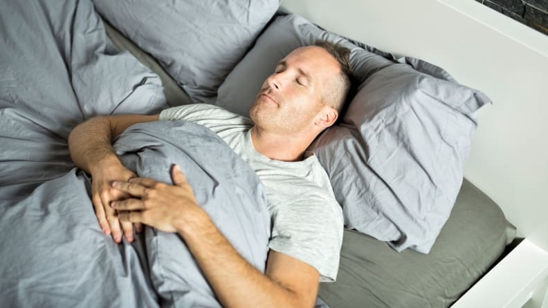 a person sleeps on their back in bed on gray sheets