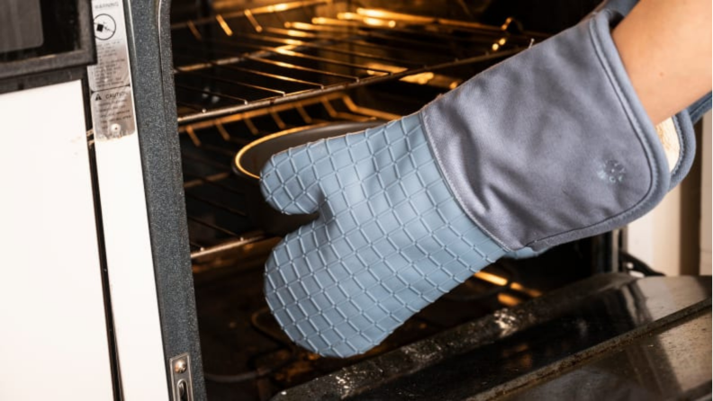 Set of arms with oven mitts reaching into an oven
