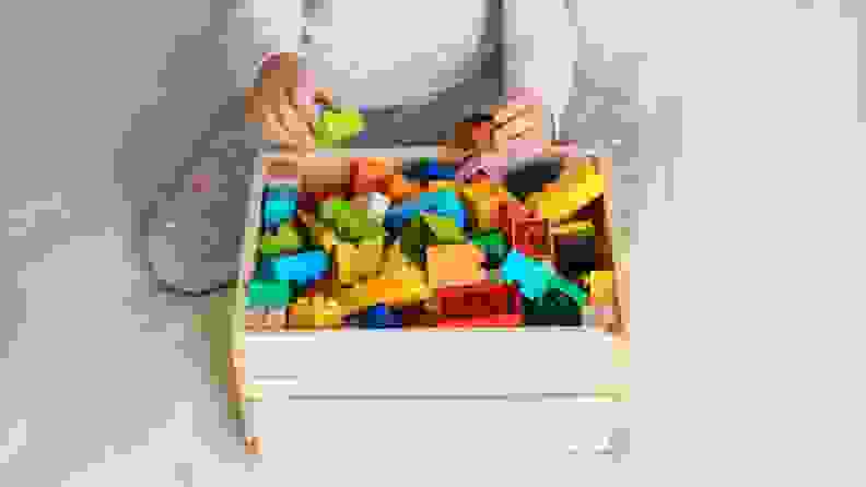 A child loads their collection of Lego Duplo blocks into a wooden crate.