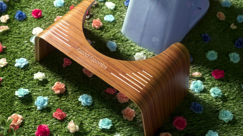 Wooden Squatty Potty sitting in front of toilet on grass surrounded by flowers.