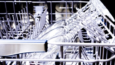 A close-up of a dishwasher's upper rack, showing wine glasses resting in stemware holders.