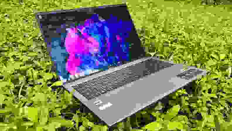 An open and powered on laptop showing a colorful screen, sitting on grass.