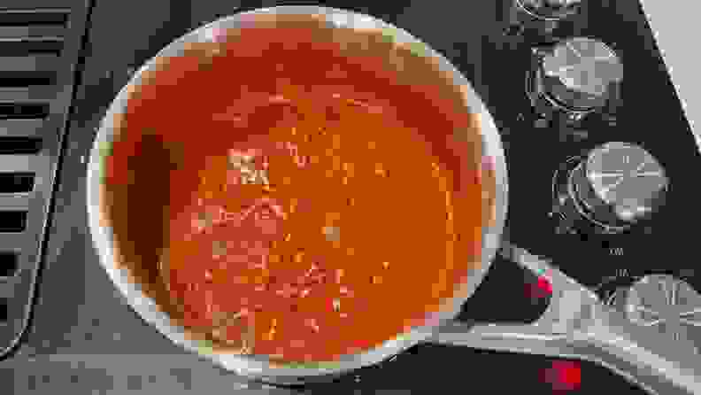 Pasta sauce inside a stainless steel pot on a black stovetop.