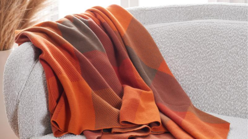 一张橙色和深红色格子毯子盖在沙发上的图片。