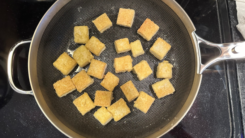 Several tofu squares being cooked inside of the Titanium Always Pan Pro on stovetop.