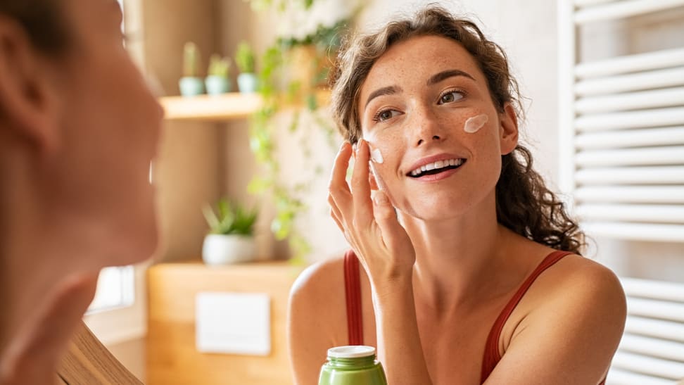 A young person looks into a mirror and applies a cream to her face.