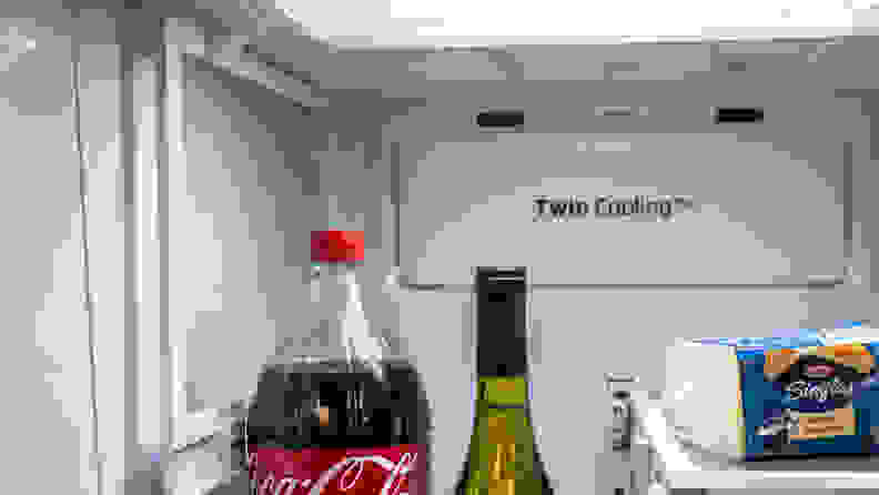 Image of one of the Samsung RF28R6301SR's flexible shelves in action. We see a coke bottle and wine bottle poking up from the bottom of the frame and off to the left a shelf is folded up, to allow both of them room to stand.