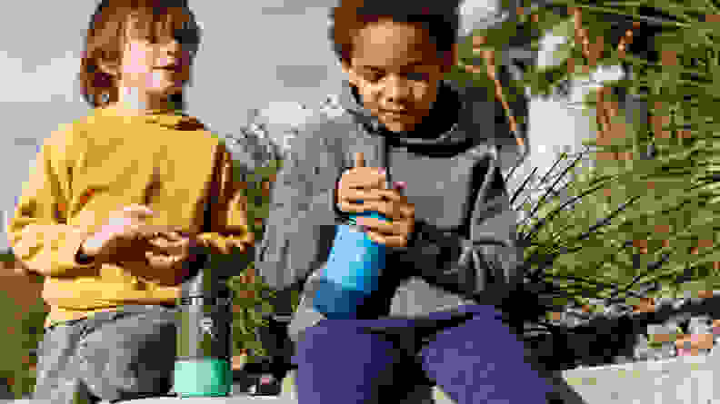 Two boys sit on a bench holding water bottles