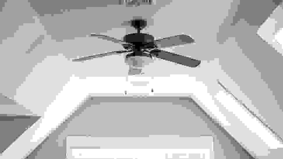 A ceiling fan hanging from a white, slanted ceiling