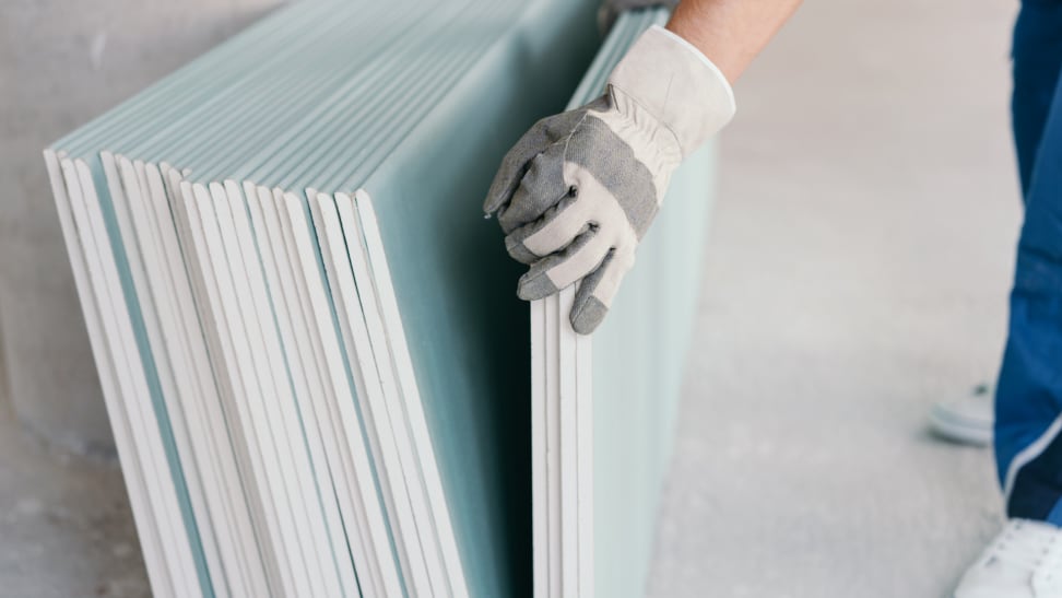 a person lifts a piece of drywall away from a stack