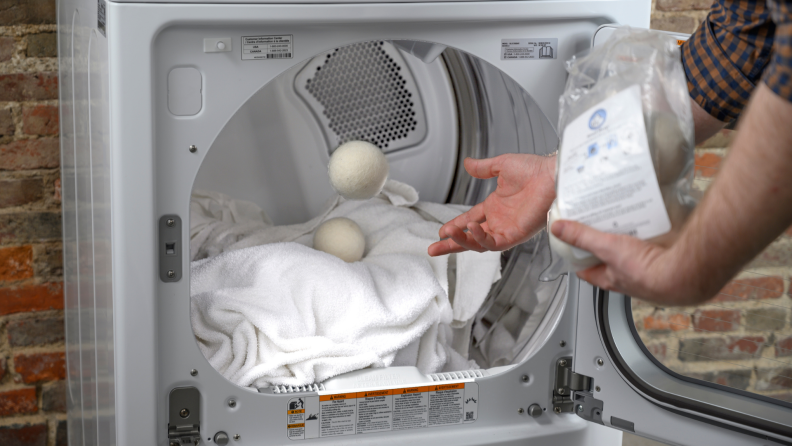 Person tossing in a wool dryer ball into a dryer with clean wet clothes