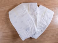 Three white Pampers Amore diapers fanned out on a wooden surface