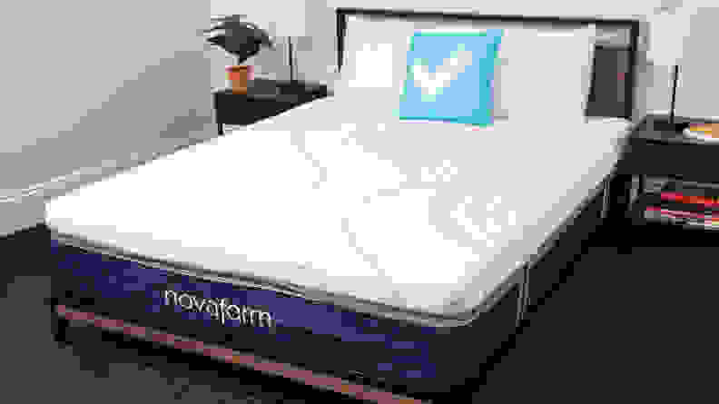 A made-up bed with white pillows and a blue checkmark pillow in a bedroom.