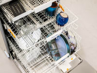 The Miele G5058 SCVi SFP stainless steel dishwasher opened to reveal three rows of white rolling dish racks near top, middle and bottom with assorted dishes inside.