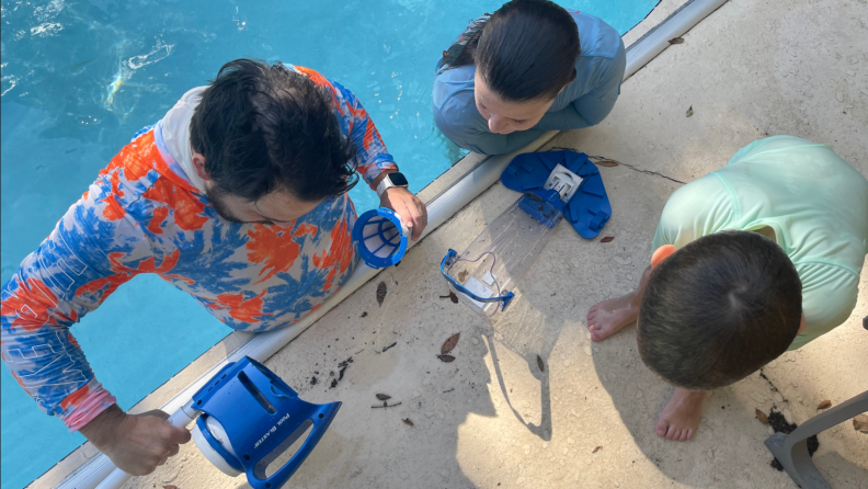 Family of three closely examine the interior filter on the Pool Blaster Rechargeable Pool Vacuum.