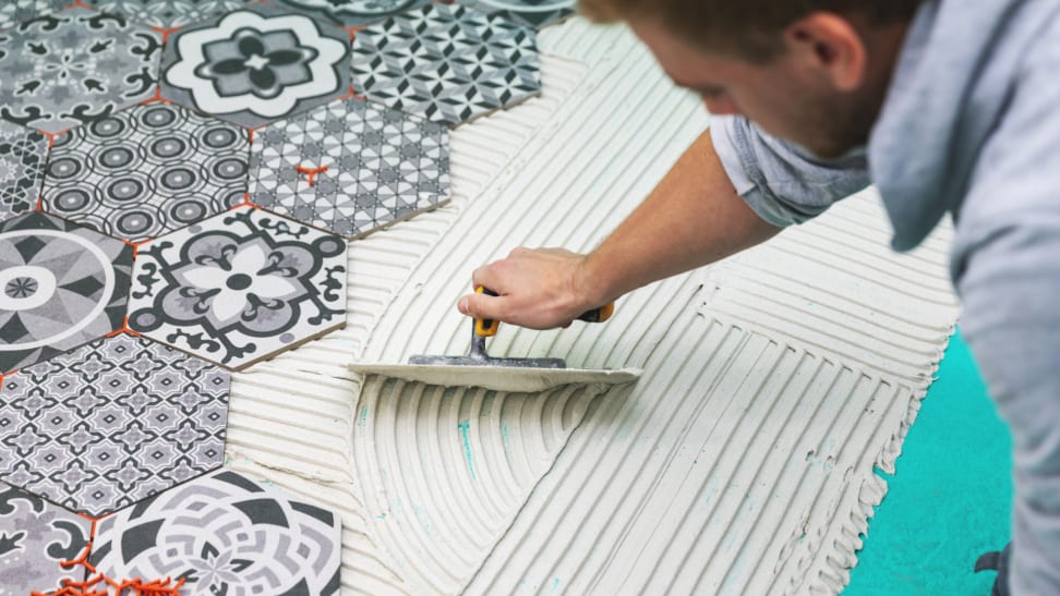 Person smoothing grout on floor as they install black and white patterned floor tiles.