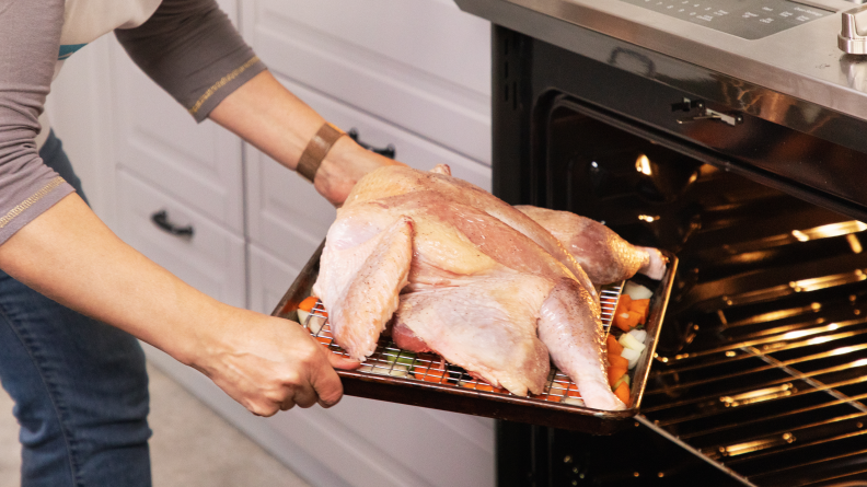 A person putting a spatchcock turkey on baking sheet into the oven.