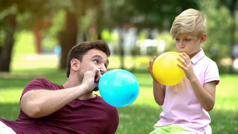 Father and son blowing up balloons outside