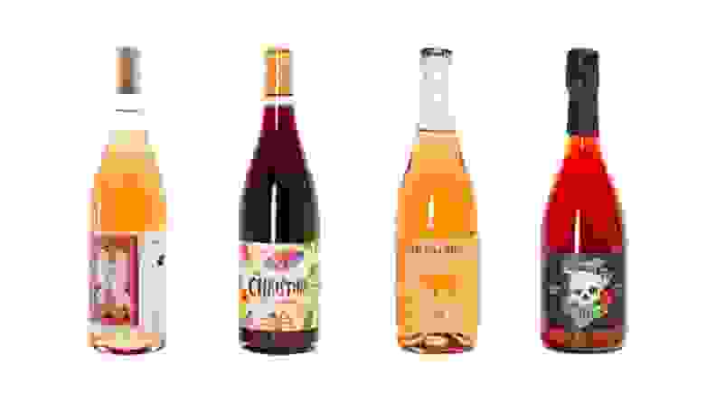 Four bottles of brightly colored natural wine bottles against a white background.