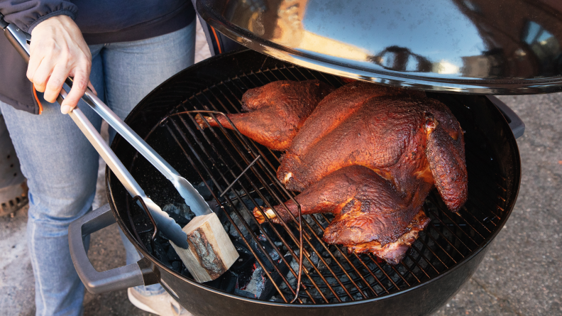 The lid of a smoker lifted to reveal a smoked spatchcocked turkey.