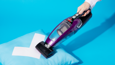 Demonstrating the purple Bissell Pet Hair Eraser 2390 vacuum on a pillow (which features our Reviewed checkmark logo).