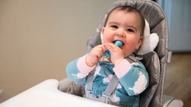 A baby in a high chair licking a spoon.