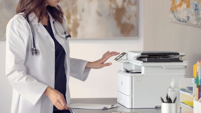 A woman in a medical lab coat reaches toward the touchscreen of an HP LaserJet Pro MFP 4101fdw.