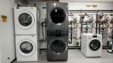 The Electrolux ELTE7600AT laundry center sits in the Reviewed lab for testing; it is shown with multiple other appliances and a wall of pipes.