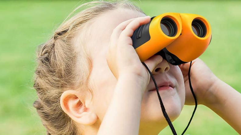 A young child looks into the sky with binoculars.