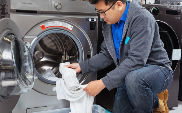 An Asian man pulls white socks and towels out of a washing machine