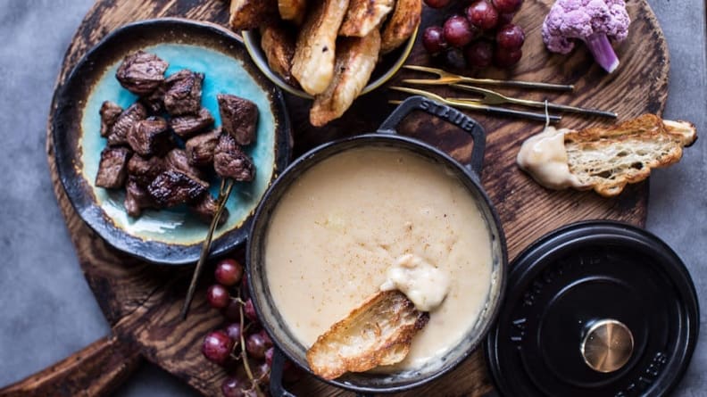 Tazón de fondue de queso pegajoso en tabla de cortar de madera con acompañamiento