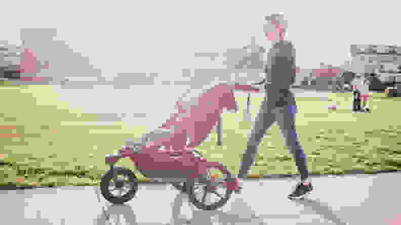 A woman pushing a jogging stroller with a child riding inside.