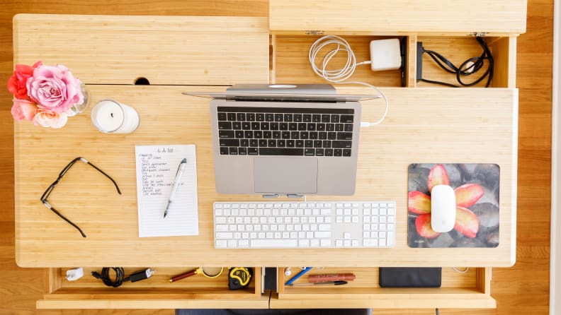 The top of a desk showing a computer, a pair of glasses, and a vase of flowers