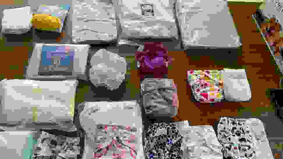 Several packages and patterns of cloth diapers stacked in neat piles with different sized inserts and pads.