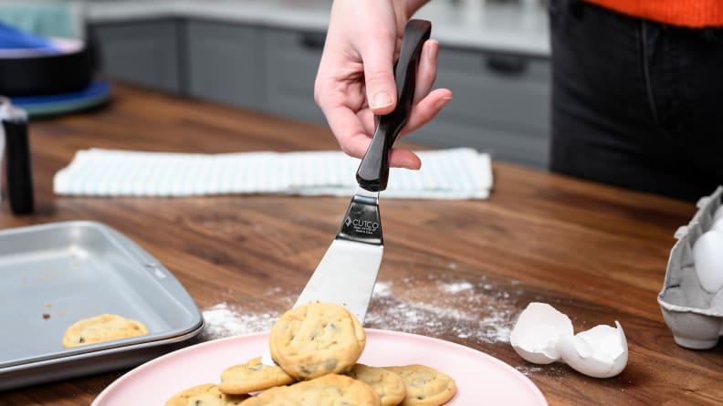 A hand moving a cookie onto a plate with a metal spatula