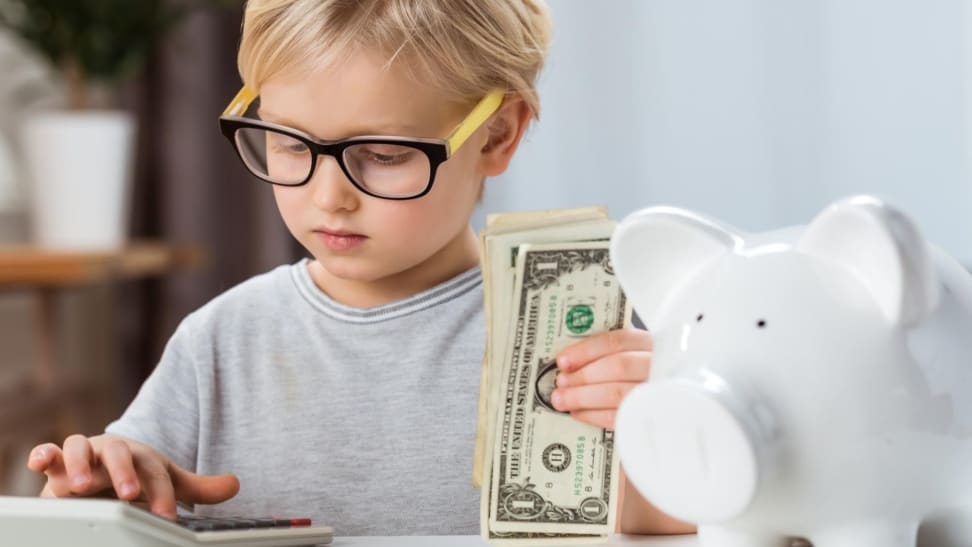 Boy with glasses counting dollar bills with adding machine.