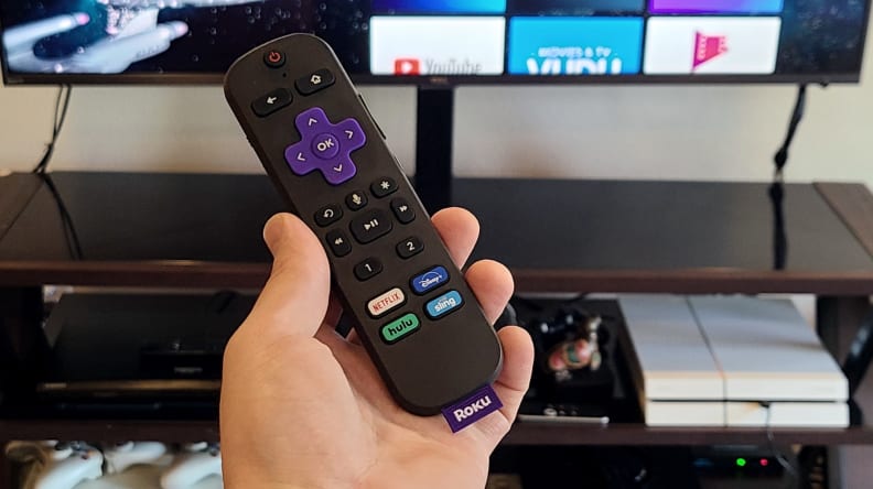 The Roku Voice Remote Pro black remote is held before an OLED display with stars strewn across the background, bearing multiple streaming and control keys.