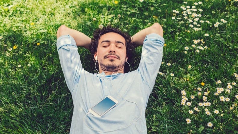 a man lies on his back in the grass meditation with earbuds