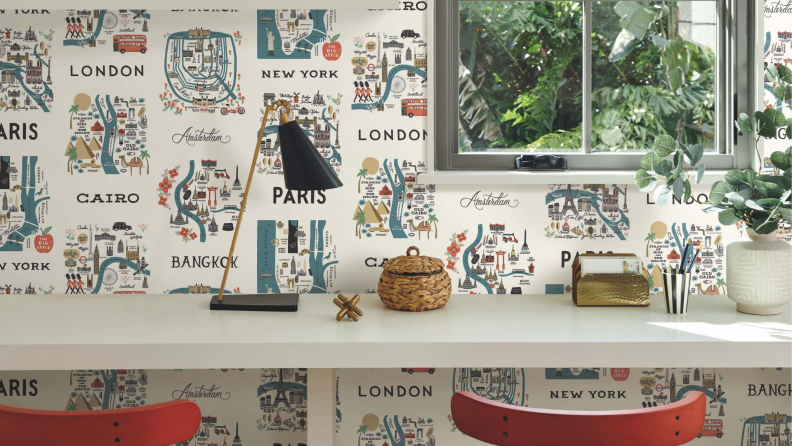 A desk with two red chairs with a wallpaper displaying miniature illustrations of cities