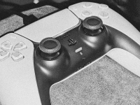 A white Sony PlayStation 5 wireless controller rests on the chair of an arm. A USB cable is plugged into the top of it for charging purposes.
