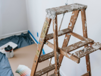 A paint-splattered ladder and drop cloth next to a white wall