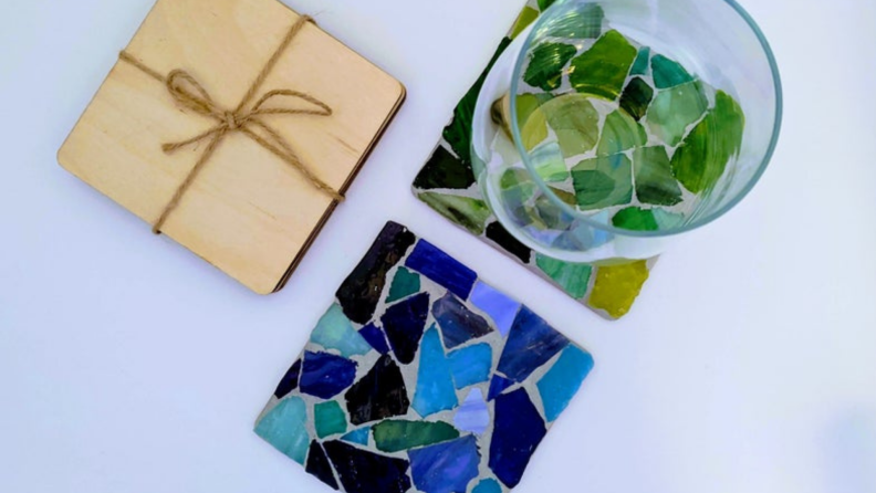Green and blue mosaic coasters with a glass cup on one next to a coaster wrapped with string