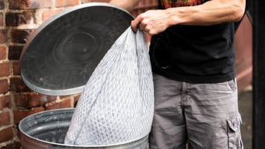 A person putting a trash bag inside of a garbage can.