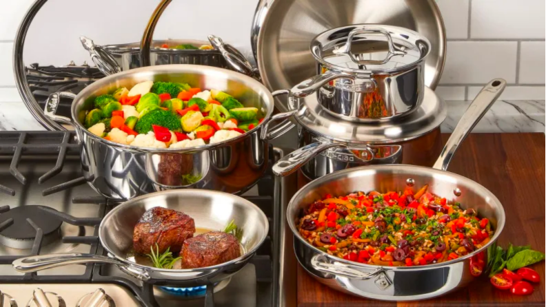 Various pots on a stove holding mixed vegetables, two steaks, and a tomato mixture.