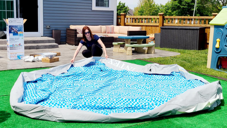 A person stretches out the Intex above-ground pool base in a backyard.