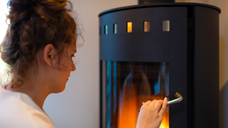 Person tending to fire inside of wood stove.