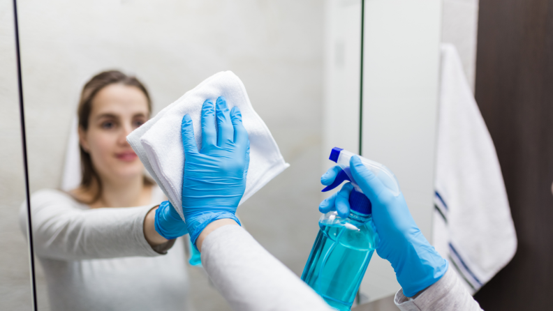 Woman using rubber gloves and a microfiber cloth to wipe off mirror.